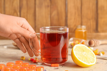 Woman with glass cup of tea for sore throat on table near wooden wall, closeup