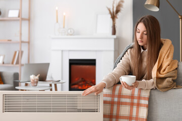Young woman with cup of hot beverage sitting on sofa at home