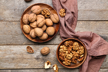Plates of whole and peeled walnuts on wooden background