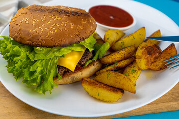 Homemade imperfect burger with potatoes and salad on a plate. Food on the table in a white plate on a wooden board