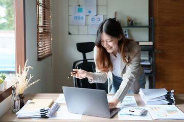 financial, Planning, Marketing and Accounting, portrait of Asian employee checking financial statements using documents and computer laptop at work
