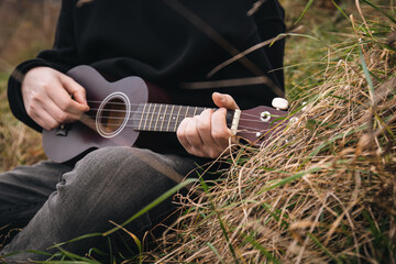 A man plays the ukulele guitar in nature, sitting on the grass.