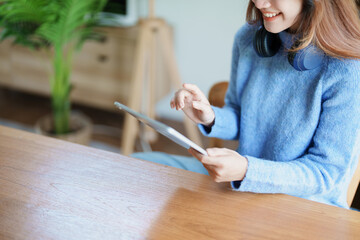 Portrait of a teenage Asian woman using a tablet, wearing headphones to study online via video conferencing on a wooden desk in library