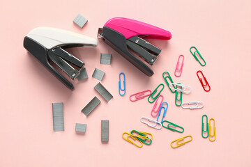 Office staplers, staples and paper clips on pink background