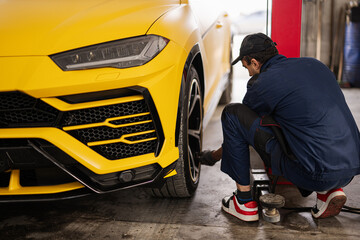 Fototapeta na wymiar Mechanic checks tire pressure in yellow sport car suv.