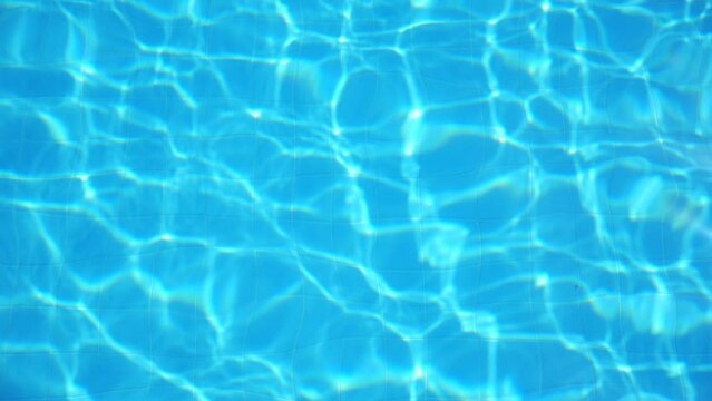 Crystal clear water with rippling sunlight in swimming pool. Bright sun beams reflecting and sparkling on surface of aqua. Beautiful background. Slow motion Close up Top view