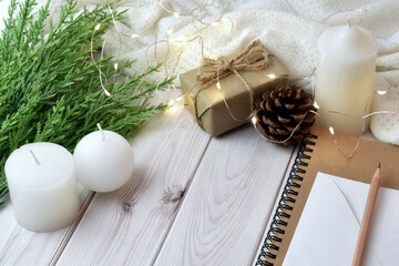 Fototapeta na wymiar Happy festival concept with brown gift box on white plank floor Decorated with candle, pine leaves, notebook, white fabric and string lights.