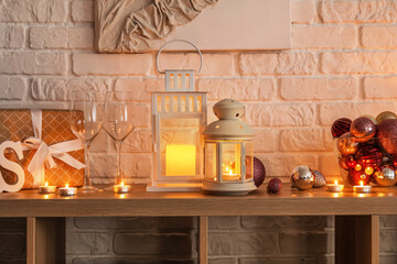 Christmas lanterns with glasses, gift and balls on shelf near white brick wall