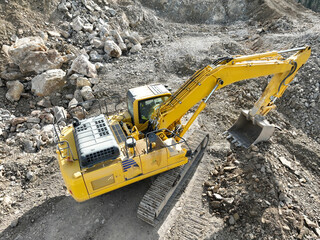 Industrial mine excavators are digging the soil in the construction site and loading trucks. Aerial drone top view. 
