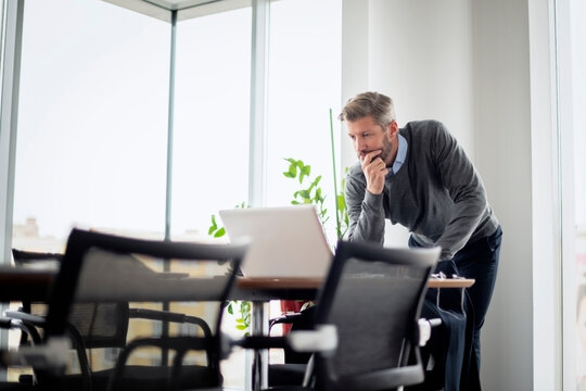Thinking businessman using laptop at the office. Care-worn business professional standing at table and having a video call at the office.