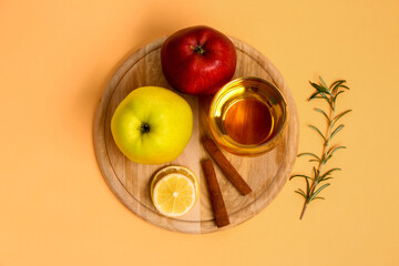 Wooden board with fresh apples, glass of juice and cinnamon sticks on color background
