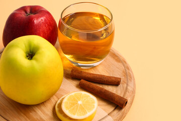 Wooden board with fresh apples, glass of juice and cinnamon sticks on color background, closeup