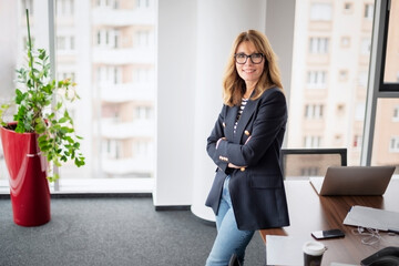 Portrait of middle aged smiling business woman. Female executive with medium-length blond hair wearing eyeglasses and businesswear and standing in a modern office.