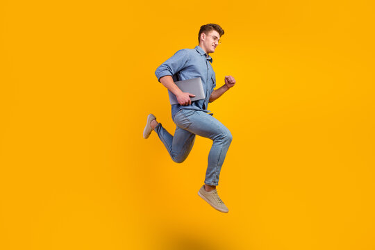 Full length photo of cheerful caucasian smart young man holding laptop smiling jumping high running on isolated bright background
