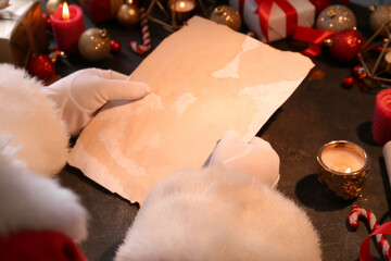 Santa Claus holding blank letter on black table with Christmas decor, closeup