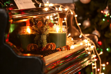 Burning candle with Christmas treats, decor and glowing lights on piano keys, closeup