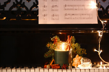 Burning candle with Christmas treats, decor and glowing lights on piano keys, closeup