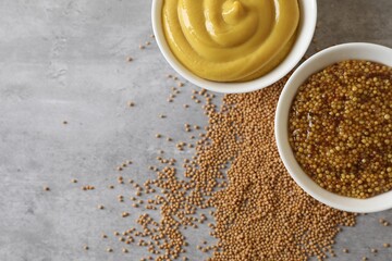 Bowls with mustard and seeds on grey table, flat lay. Space for text