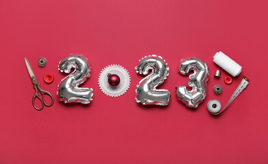 Figure 2023 made of balloons with sewing supplies and Christmas ball on red background - obrazy, fototapety, plakaty