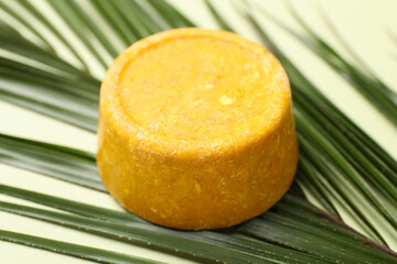 Orange solid shampoo bar and leaf on green background, closeup. Hair care