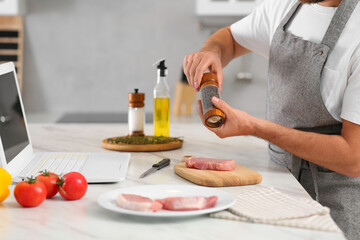 Man making dinner while watching online cooking course via laptop in kitchen, closeup