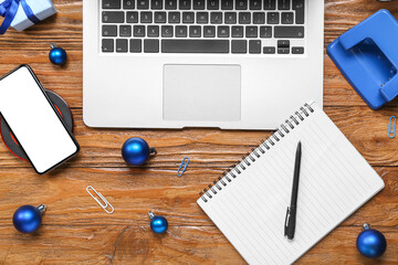 Mobile phone with laptop, office stationery and Christmas balls on wooden background