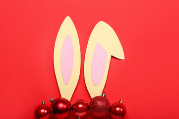 Paper bunny ears with Christmas balls on red background
