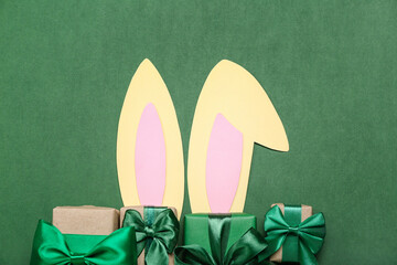 Paper bunny ears with Christmas gifts on green background