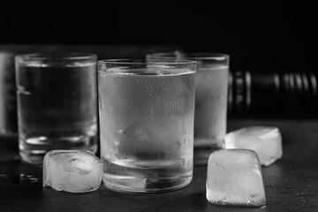 Vodka in shot glasses with ice on table against black background, closeup