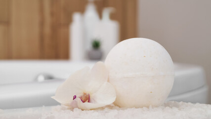 Bath bomb with orchid and sea salt on table in bathroom, closeup