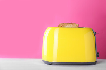Modern toaster with slices of roasted bread on white wooden table. Space for text