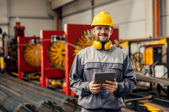 A Heavy Industry Worker Is Using Tablet In Factory While Smiling A The Camera.