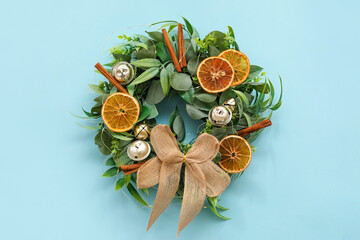 Beautiful Christmas wreath decorated with bells, orange slices and cinnamon on color background