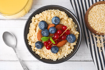 Bowl of delicious cooked quinoa with almonds, cranberries and blueberries on white wooden table, flat lay