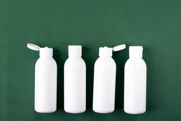 Four white cosmetic bottles on green background. Unlabeled body care and skin care product. Travel container set for beauty products. Copy space