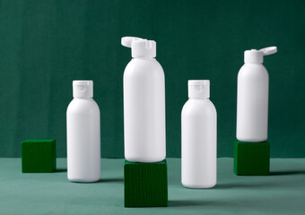 Four white cosmetic bottles on green background with cube podiums. Body care, skin care or pharmacy product. Travel container set for beauty products