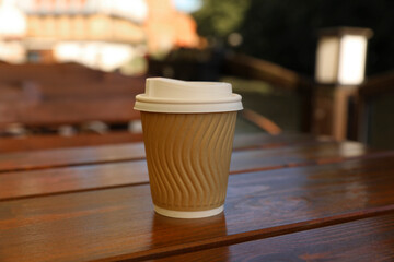 Takeaway paper cup with coffee on wooden table outdoors