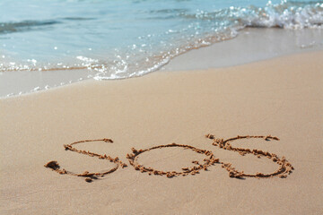 Message SOS drawn on sandy beach near sea