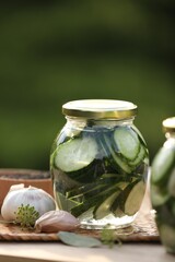 Jar of delicious pickled cucumbers and ingredients on wooden table against blurred background