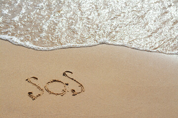 Message SOS drawn on sandy beach near sea