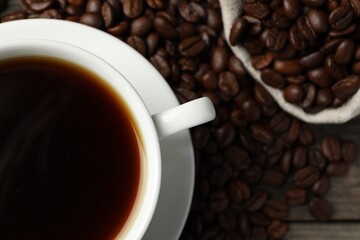 Cup of aromatic coffee and beans on wooden table, flat lay. Space for text