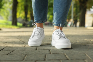 Woman in stylish sneakers walking on city street, closeup