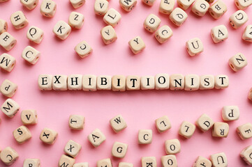 Word EXHIBITIONIST made with wooden cubes on pink background, flat lay