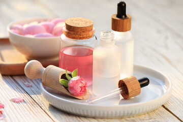 Fototapeta na wymiar Bottles of rose essential oil and flowers on white wooden table