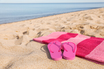 Fototapeta na wymiar Beach towel and slippers on sand near sea, space for text