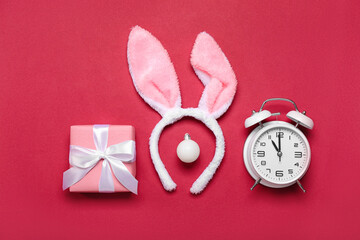 Bunny ears with Christmas ball, gift and alarm clock on red background