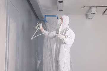 Decorator dyeing wall in grey color with spray paint indoors