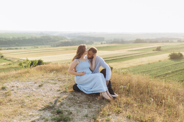 Naklejka na ściany i meble Portrait of a lovely couple standing together on the greenfield. Happy couple expecting a baby, young family concept