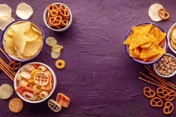 Salty snacks, overhead flat lay background with copy space. Party food frame. Potato and tortilla chips, salt crackers and other appetizers in bowls