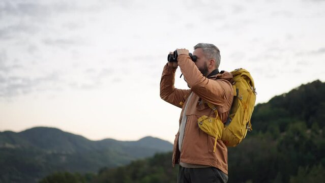 Male hiker looking through binoculars in nature.